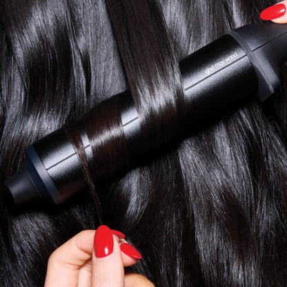Person using a black hair straightening device on dark hair with red nail polish.